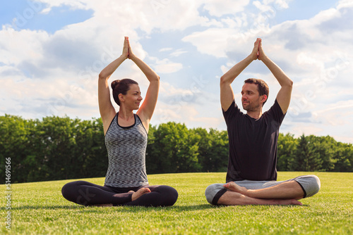 Young healthy man and woman doing yoga in the sunny summer park. Fitness and healthy lifestyle