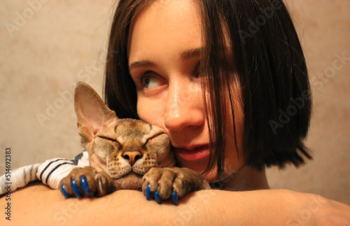 A young beautiful woman cuddling, hugging beloved bald Canadian Sphynx naked hairless cat with silicone fingernails. The owner and happy calm kitty are happy together. Feline pet care, love concept.