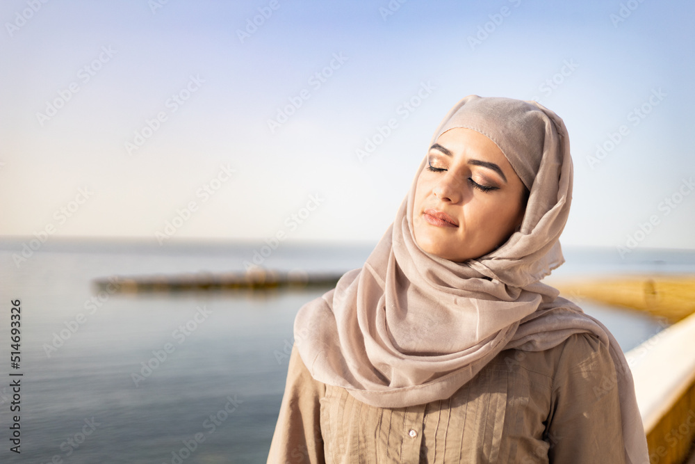 Muslim and modern woman closing eyes on the beach with hope and happiness Muslim and modern woman closing eyes on the beach with hope and happiness