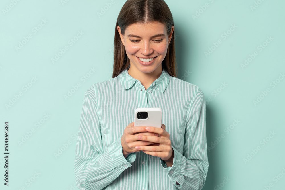Smiling charming Caucasian student girl using mobile phone isolated over blue background Smiling charming Caucasian student girl using mobile phone isolated over blue background