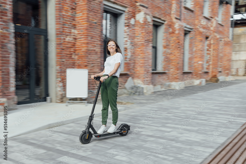Woman in white t shirt and sneakers rides electric scooter Woman in white t shirt and sneakers rides electric scooter