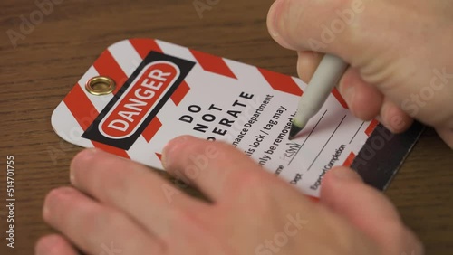 A close up view of a repair worker filling in a lockout/tagout tag before servicing a piece of machinery.
 photo