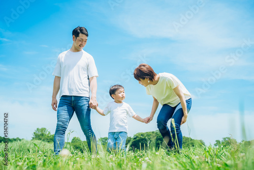 手を繋いで晴天の緑地を歩く親子3人 © maru54