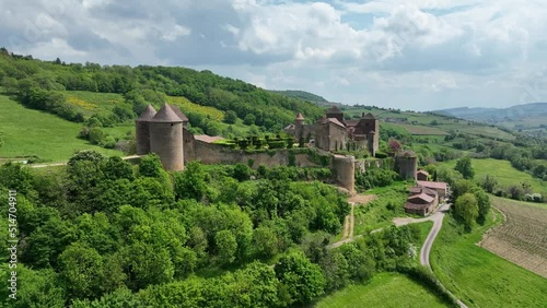 Aerial panning shot of Berze le chatel feudal medieval castle with double enclosure of walls, round towers, donjon, fortified gatehouse on a hill in Central France