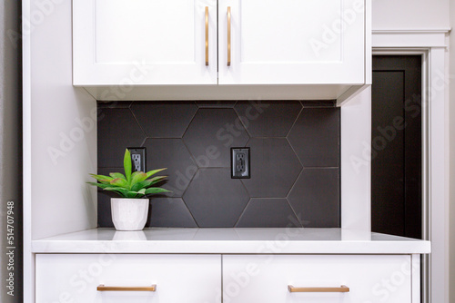 A modern farmhouse kitchen with white cabinets, black hexagon tile backsplash and and gold pulls.
