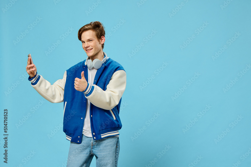 Fototapeta premium handsome stylish young man takes a selfie on the phone with his arm outstretched while standing with headphones around his neck
