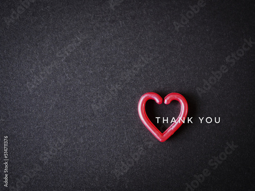The words "thank you" message and red heart on the black paper background. top view, flat lay with copy space. Greeting card..