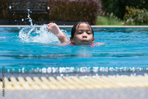 Little girls enjoy swimming in the pool. Cute Asian girl wearing a life jacket is having fun playing in the outdoor pool. Healthy Summer Activities for Kids. © scentrio
