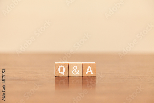 Q&Aの文字。質問と回答。question and answer。3つの木製ブロックに書かれている。白い文字。木製テーブルと白い壁紙の背景。