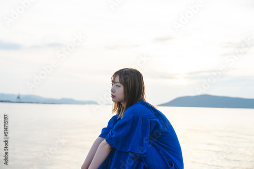 夕暮れの海にいる青いワンピースの女性