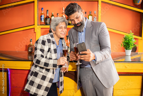 Happy indian business people holding glass of wine and champagne in hand and using smart phone , Young man and senior woman corporate party to celebrate company success.