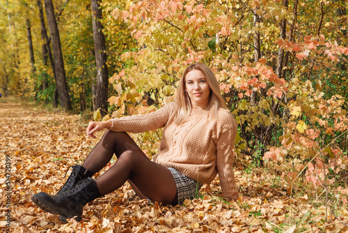 A beautiful young woman sitting in a forest on a dry autumn leaves.