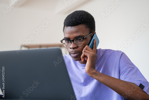 Serious black businessman talk on the phone, using laptop in office room