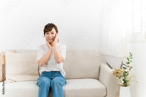 ソファで肌を触ってスキンケアする日本人女性（保湿・美容） 