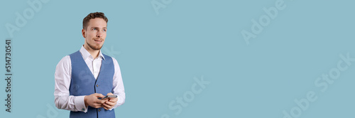Bearded business man with phone in his hand posing in white shirt and blue vest on a blue background in the studio, business people concept