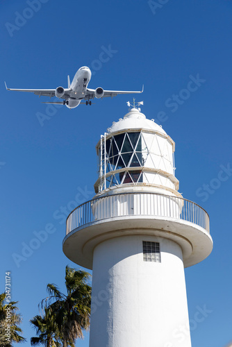 旅、青空を背景に白い灯台の上を通過する旅客機