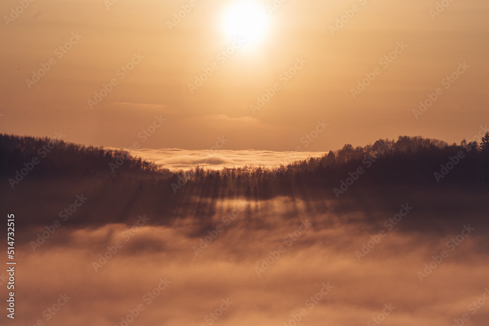 View of the sunset over a sea of clouds with a view of the sun passing through the forest on the other hill. Palkovicke hurky, moravskoslezský region, czech republic