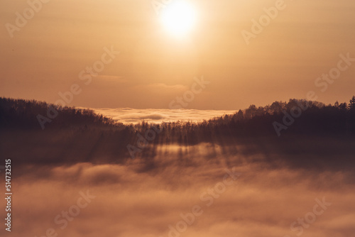 View of the sunset over a sea of clouds with a view of the sun passing through the forest on the other hill. Palkovicke hurky, moravskoslezský region, czech republic