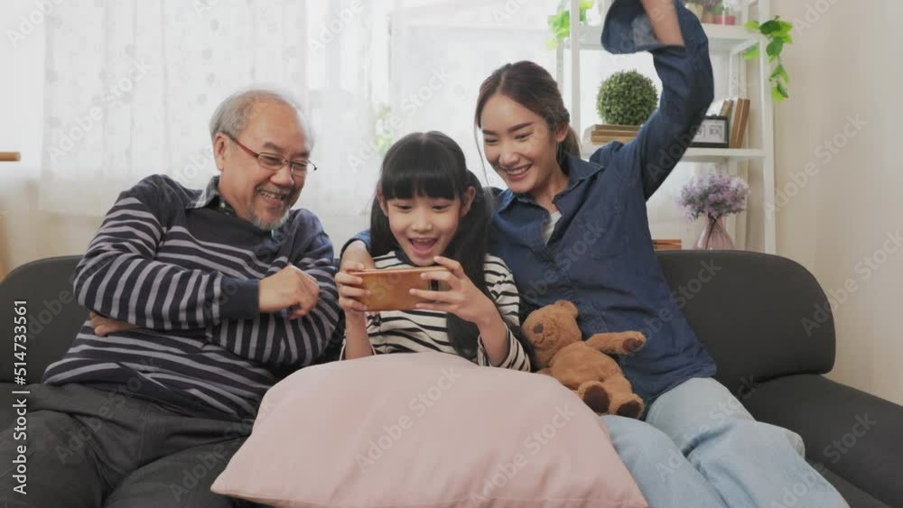 Asian happy family play time. little girl with grandparents together playing video games use joystick control enjoy laughing fun in living room home at night. Happy child happiness lifestyle concept. Asian happy family play time. little girl with grandparents together playing video games use joystick control enjoy laughing fun in living room home at night. Happy child happiness lifestyle concept.
