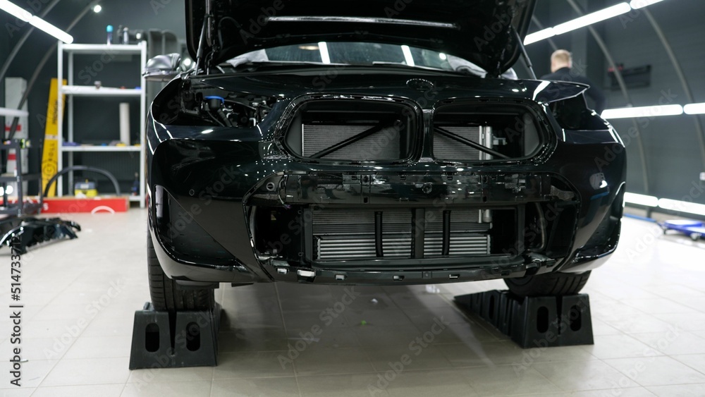 Fototapeta premium Car detailing. A black car without a bumper, prepared for pasting with a protective film. Disassembled car, ready for pasting with a protective film. A car without a bumper.