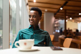 Portrait of handsome young black man in coffee shop looking through window