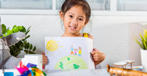 Happy child little girl lift up colorful drawing family standing hold hands on planet earth on paper to camera, Asian cute kid preschool smiling showing draw picture at home earth day concept