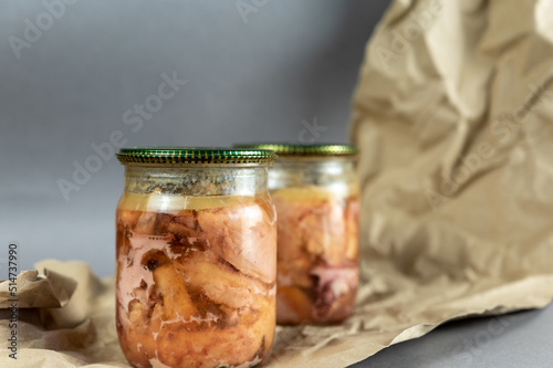 A glass jar of canned meat. Homemade chicken stew against a gray background. Slices of appetizing meat tightly packed in a transparent jar. Food ready to eat. Close-up. Selective focus.