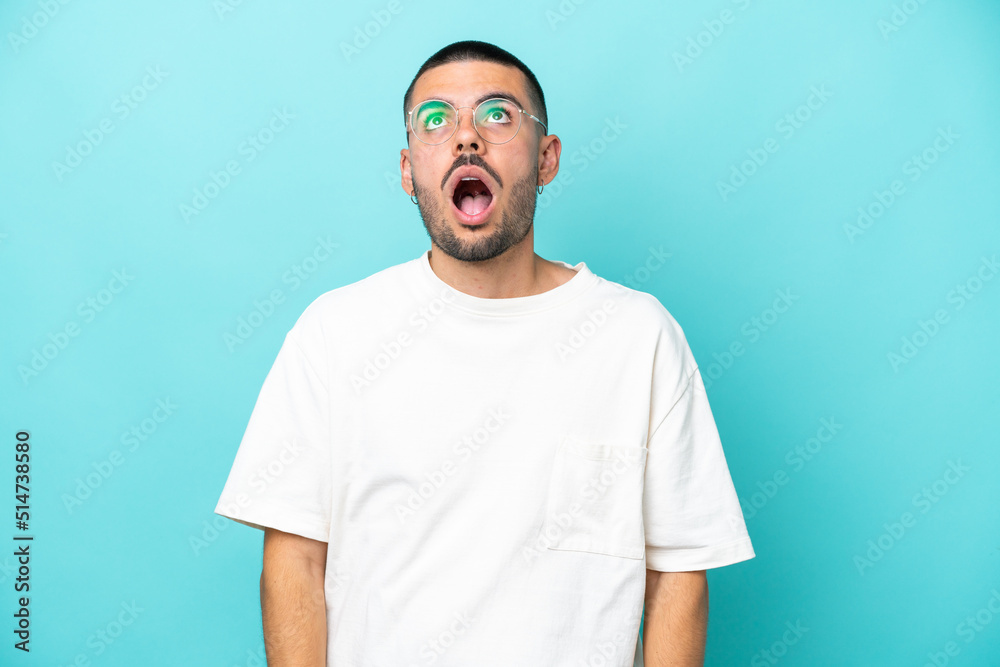 Young caucasian man isolated on blue background looking up and with surprised expression Young caucasian man isolated on blue background looking up and with surprised expression