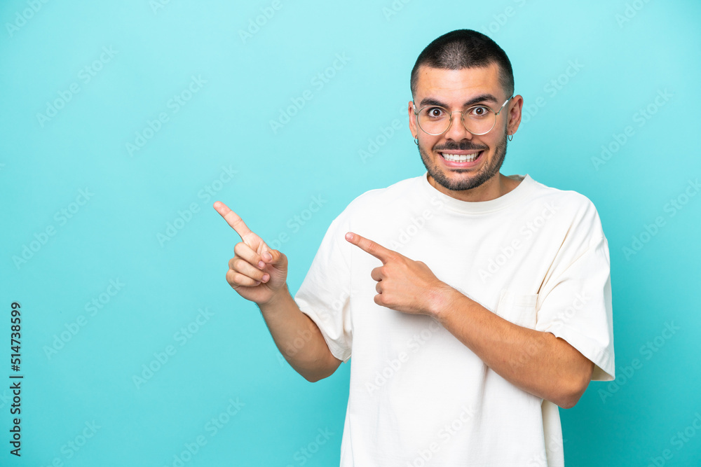 Young caucasian man isolated on blue background frightened and pointing to the side Young caucasian man isolated on blue background frightened and pointing to the side