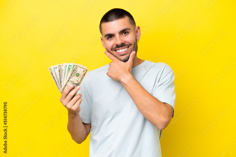 Young caucasian man taking a lot of money isolated on yellow background happy and smiling Young caucasian man taking a lot of money isolated on yellow background happy and smiling