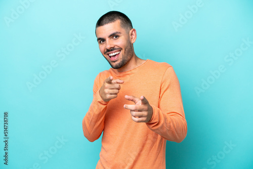 Young caucasian man isolated on blue background pointing to the front and smiling