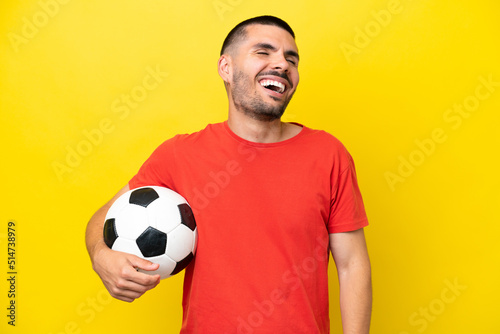 Young caucasian man playing soccer isolated on yellow background laughing