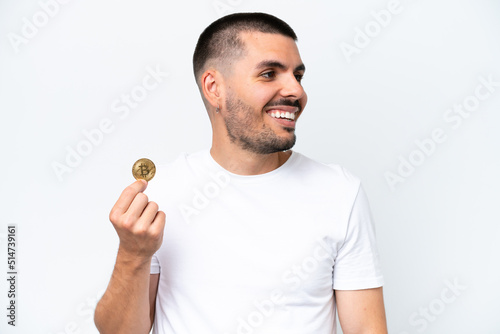 Young caucasian man holding a bitcoin isolated on white background looking side