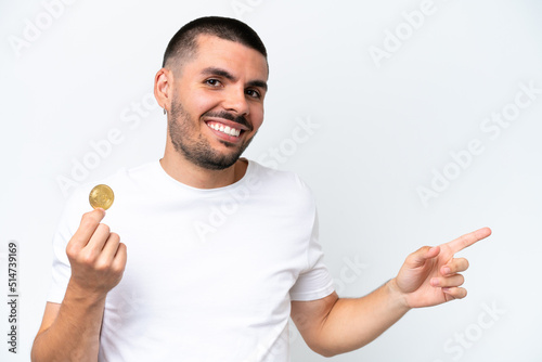 Young caucasian man holding a bitcoin isolated on white background pointing finger to the side