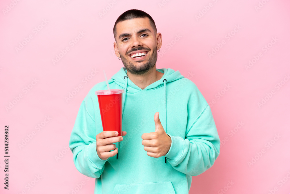 Young caucasian man holding soda isolated on pink background giving a thumbs up gesture Young caucasian man holding soda isolated on pink background giving a thumbs up gesture