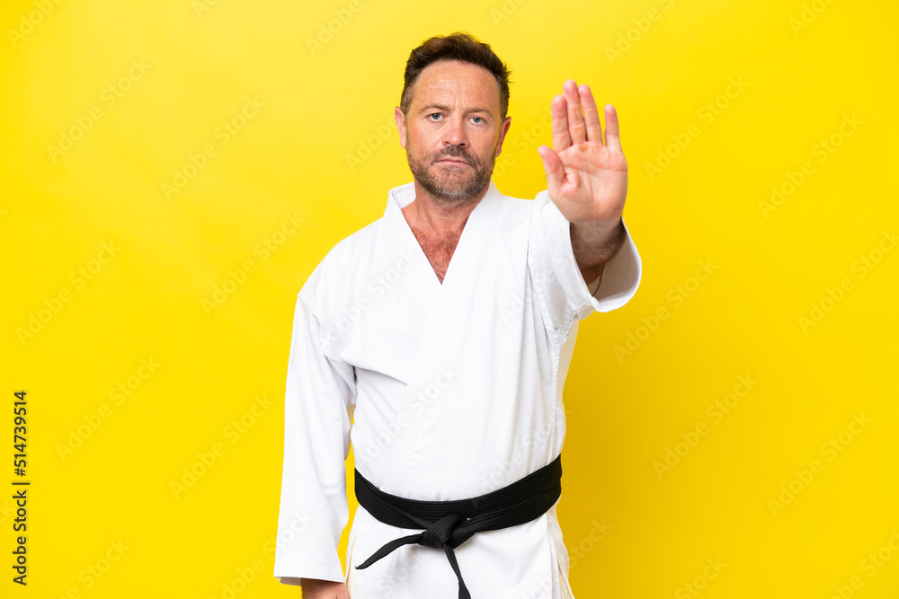 Middle age caucasian man doing karate isolated on yellow background making stop gesture Middle age caucasian man doing karate isolated on yellow background making stop gesture