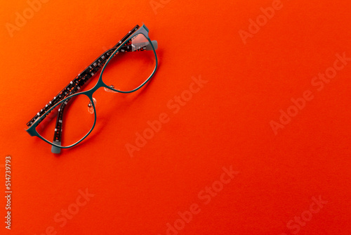 Stylish eyeglasses over orange background. Glasses selection, eye test, vision examination at optician, fashion accessories concept. Top view, flat lay.