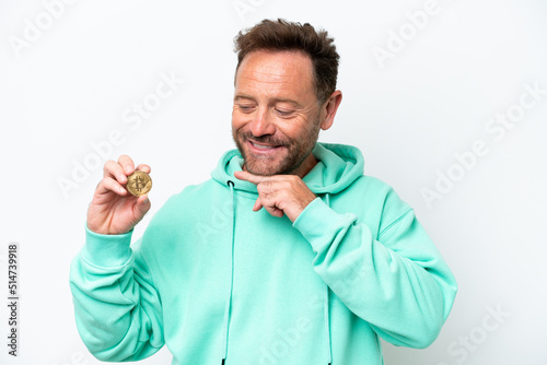 Middle age man holding a Bitcoin over isolated background looking to the side and smiling