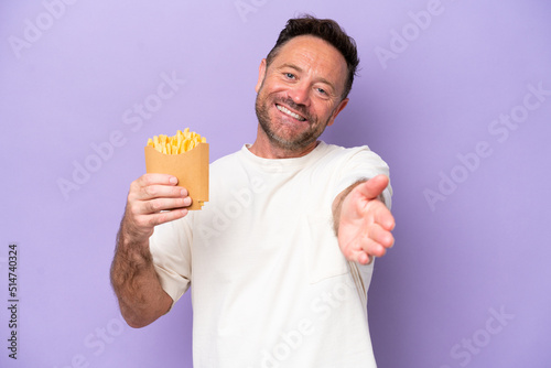 Middle age caucasian man holding fried chips isolated on purple bakcground shaking hands for closing a good deal © luismolinero