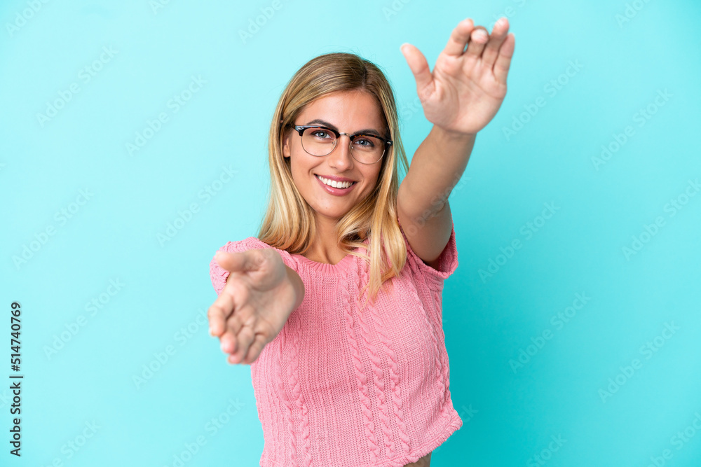 Fototapeta premium Blonde Uruguayan girl isolated on blue background presenting and inviting to come with hand