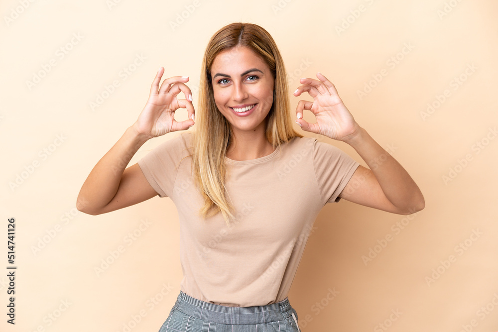 Blonde Uruguayan girl isolated on beige background showing ok sign with two hands Blonde Uruguayan girl isolated on beige background showing ok sign with two hands