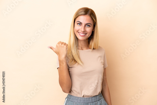 Blonde Uruguayan girl isolated on beige background pointing to the side to present a product © luismolinero