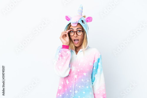 Blonde Uruguayan girl wearing a unicorn pajama isolated on white background with glasses and surprised