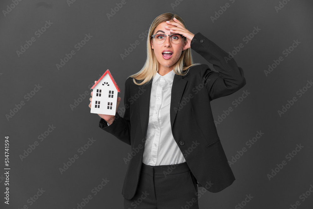 Blonde Uruguayan girl holding a house toy isolated on black background with surprise expression Blonde Uruguayan girl holding a house toy isolated on black background with surprise expression