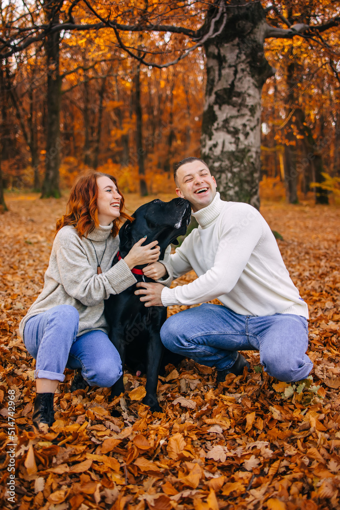 Happy young family man and woman have fun walking with their dog in the autumn park, they adore their pet. Happy young family man and woman have fun walking with their dog in the autumn park, they adore their pet.