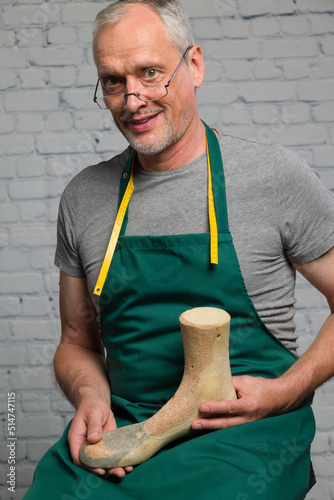 happy shoemaker wearing a green apron is presenting an individual made wooden last to make an individual crafted orthopedic shoe