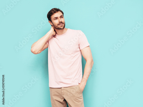 Portrait of handsome smiling stylish hipster lambersexual model. Sexy man dressed in pink T-shirt and trousers. Fashion male isolated on blue wall in studio