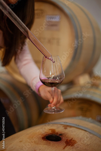 winemaker woman takes a sample of wine from a barrel and pours a little into a glass with special tool