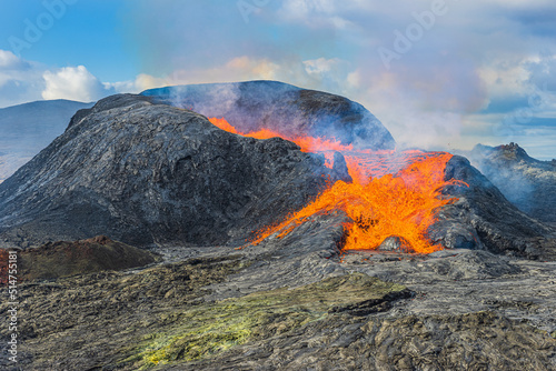 Eruption of an active volcano on the Reykjanes Peninsula. strong lava flow from a volcanic crater in Iceland. liquid magma from crater at day in sunshine with clouds and blue sky.