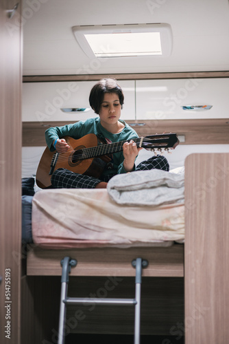 Girl playing guitar on the bed of the caravan